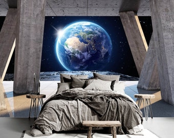 May include: A bed with gray and brown bedding sits in a room with concrete pillars. The room has a large window that looks out onto a view of Earth in space.