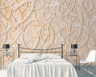 May include: A white bed with a white bedspread sits in front of a wall with a beige and white intricate pattern. The pattern is reminiscent of a traditional Islamic design. Two black lamps with white shades sit on end tables on either side of the bed.