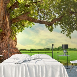 May include: A white bed with a white bedspread sits in front of a wall mural depicting a large, old tree with green leaves and a bright blue sky with white clouds. The tree is in front of a green field.