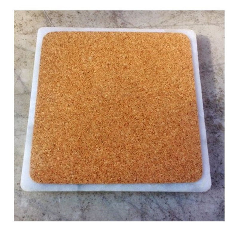 May include: A square cork trivet with a white marble border.