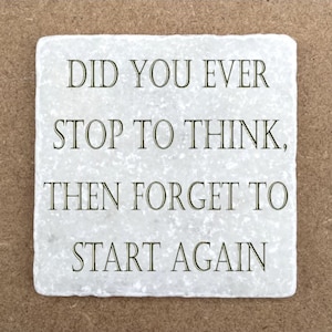 May include: A square, off-white stone coaster with the text "DID YOU EVER STOP TO THINK, THEN FORGET TO START AGAIN" in dark grey lettering. The coaster has a slightly textured surface.