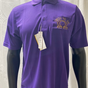 May include: A purple polo shirt with short sleeves and a three-button placket. The shirt features the embroidered text "OMEGA PSI PHI" in gold thread on the left chest. A white tag hangs from the shirt.