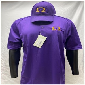 May include: A purple polo shirt and matching baseball cap. Both items feature a gold embroidered Omega symbol. The shirt has a three-button placket and a small pocket on the chest. A price tag hangs from the shirt.