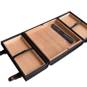 May include: Black leather cigar humidor with a wooden interior. The humidor has multiple compartments and a built-in humidifier. The humidor is open, revealing the interior. The humidor has a rectangular shape and is designed to store cigars.
