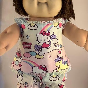 May include: A Cabbage Patch Kids doll wearing a pastel Hello Kitty pajama set. The top and shorts feature Hello Kitty riding a unicorn, rainbows, and clouds. The text "Hello Kitty" is visible on the top and shorts.