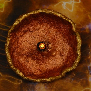 May include: A round, copper-colored dish with a raised, textured rim and a small, gold-colored jewel in the center.