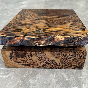 May include: A rectangular wooden box featuring a natural live edge top lid and a base with a highly detailed, swirling dark brown and golden tan wood grain pattern. The box has a smooth, polished finish that highlights the intricate organic textures.