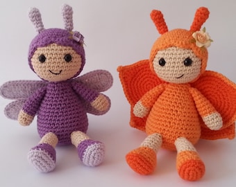 May include: Two crocheted stuffed toys shaped like butterflies. One is purple with a flower on its head and the other is orange with a flower on its head.