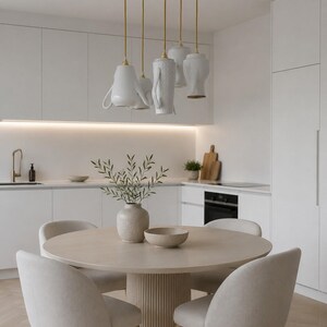 Pode incluir: Um conjunto de jantar com uma mesa redonda bege clara com base de pedestal canelada e quatro cadeiras estofadas a condizer. Sobre a mesa, um conjunto de cinco candeeiros suspensos de cerâmica branca com cabos dourados. O texto UPservies aparece.