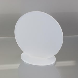 May include: A frosted white, oval-shaped decorative object. The object is supported by a small, circular base. The design is simple and minimalist, with a smooth, opaque surface. The object is likely made of glass or a similar material.
