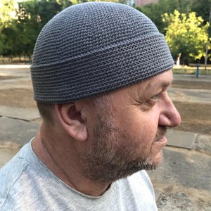 May include: A grey knitted beanie hat with a folded brim. The hat is made of a textured, woven material. The hat is worn by a person.