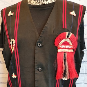 May include: A black sleeveless vest with red and blue stripes. The vest has a decorative element on the right side with red, white, and black tassels. The vest has four buttons down the front.