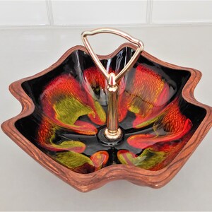 May include: A star-shaped ceramic serving dish with a gold metal handle. The dish has a black background with red, yellow, and green swirls.