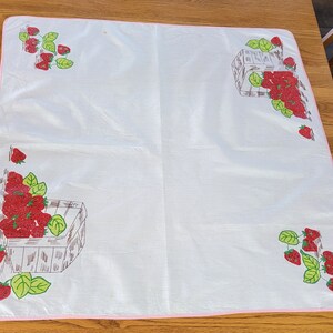May include: White tablecloth with pink trim and a strawberry design. The tablecloth features strawberries in baskets and vines with leaves.