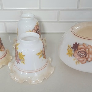 May include: Four white glass lampshades with ruffled edges and floral designs in shades of brown and cream.