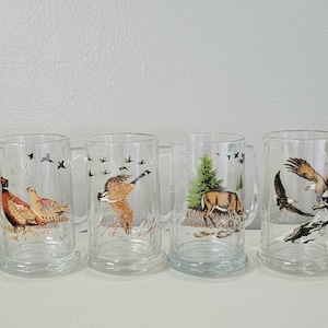 May include: Six clear glass mugs with handles, each featuring a different wildlife scene. The mugs have a white background with colorful images of a fish, a pheasant, a duck, a deer, an eagle, and a duck.