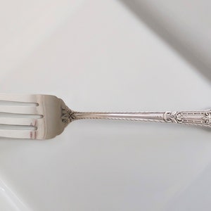 May include: A silver fork with an ornate handle. The handle has a floral design and a smooth oval in the center.