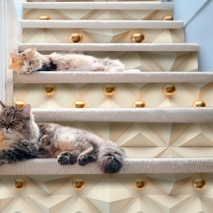May include: Two cats are relaxing on a set of stairs with a beige and gold geometric pattern. The cats are lying on the stairs, one on each step. The stairs are carpeted and have a white railing.