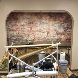 May include: A room with a brick wall mural, scaffolding, and various tools and supplies. The mural features a faded world map design.