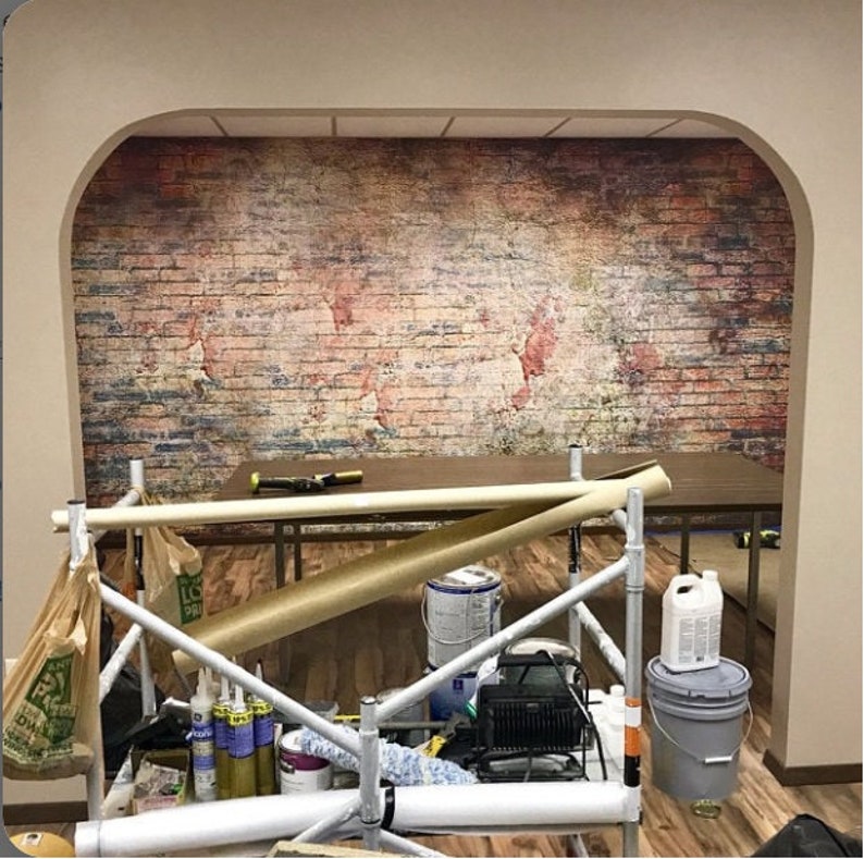 May include: A room with a brick wall mural, scaffolding, and various tools and supplies. The mural features a faded world map design.