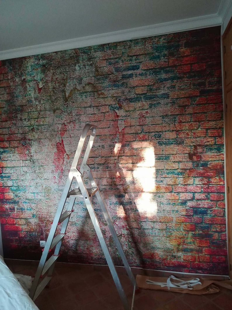 May include: A silver step ladder is positioned in front of a brick wall mural. The mural features a distressed brick pattern with shades of red, orange, blue, and green.