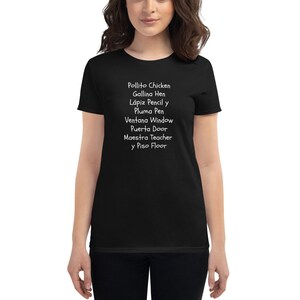 May include: Black women's t-shirt with white text that reads "Pollito Chicken, Gallina Hen, Lápiz Pencil y Pluma Pen, Ventana Window, Puerta Door, Maestra Teacher y Piso Floor".
