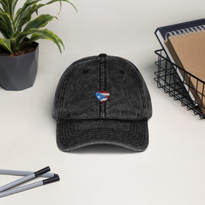 May include: A black vintage washed denim baseball cap with a small embroidered heart featuring the Puerto Rican flag.