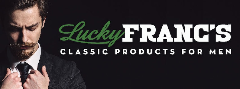 May include: A man in a black suit and tie with a beard and mustache. The text "Lucky FRANC'S CLASSIC PRODUCTS FOR MEN" is in white letters on a black background. The word "Lucky" is in green.