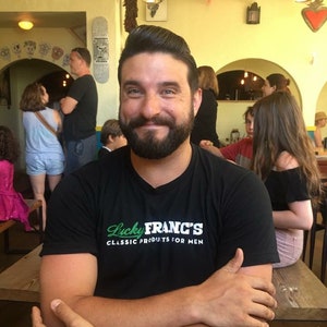 May include: A man with a beard is wearing a black t-shirt with the text "Lucky Franc's Classic Products for Men".