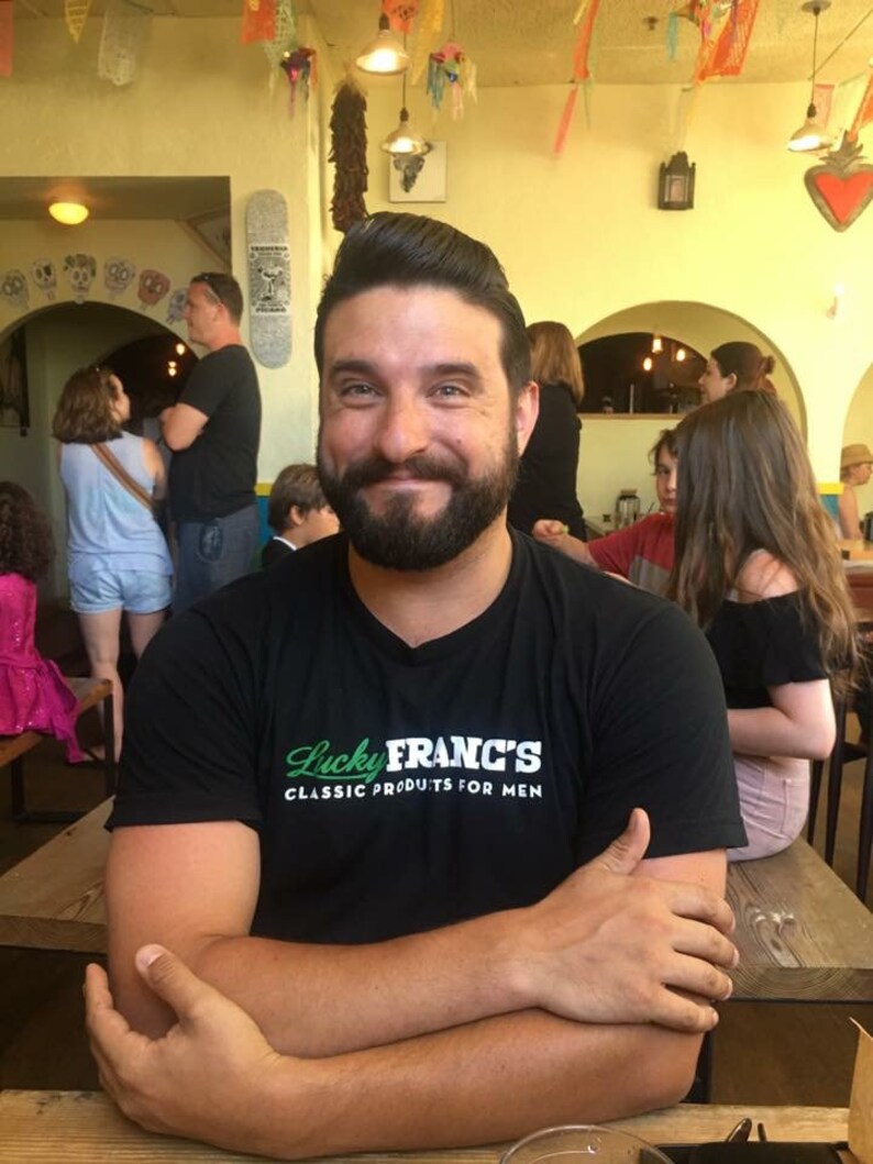 May include: A man with a beard is wearing a black t-shirt with the text "Lucky Franc's Classic Products for Men".