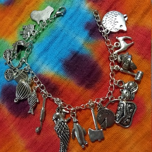 May include: A silver charm bracelet featuring a range of charms, including a hedgehog, a fish, a parrot, a penguin, an axe, a wedge of cheese, a hot air balloon, a milk carton, a carriage, a knight, a cat, and a heart.