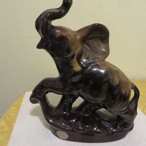 May include: A brown ceramic elephant figurine with its trunk raised in the air. The elephant is standing on a base with a brown glaze.