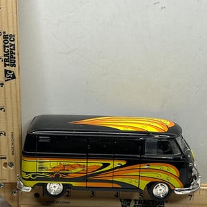 May include: Black toy van with a flame design in yellow and orange. The van has a desert landscape graphic on the side. The wheels are silver. The van is approximately 7 inches long.