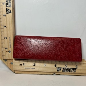 May include: A rectangular, red leather case with a textured surface. The case is approximately 6 inches long. The item is placed on a wooden ruler with the text "Tractor Supply Co."