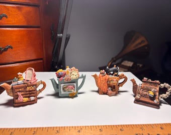 Puede incluir: Cuatro teteras en miniatura decorativas con diseños detallados. Una presenta una máquina de coser, otra un tocador y otras con varios elementos decorativos. Las teteras son marrones, verdes y naranjas, con detalles intrincados.
