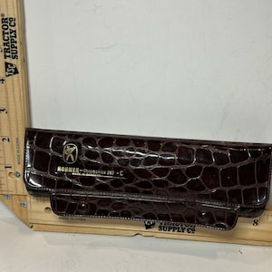 May include: A brown, faux-crocodile-skin case for a Hohner Chromonica 280-C harmonica. The case is rectangular with a flap closure and features the Hohner logo and "Made in Germany" text. The case is approximately 8 inches long.