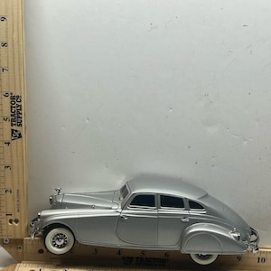 May include: A silver die-cast model car with white wall tires. The classic car has a streamlined design and is approximately 9 inches long. The model car is a collectible item.