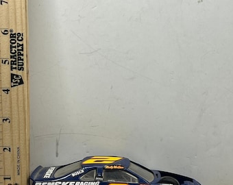 Op de afbeelding: Een blauw en geel Penske Racing modelauto met het nummer 2 aan de zijkant. De auto heeft sponsorlogo's en de naam "Rusty Wallace" op het dak. Het model is ongeveer 15 cm lang.