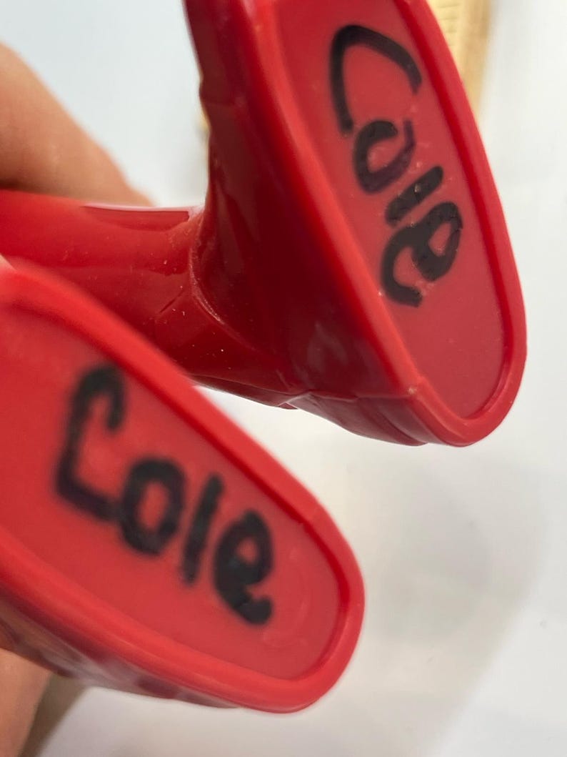 May include: Close-up of two red plastic objects with the name "Cole" written in black marker on each. The objects appear to be part of a larger item, possibly a toy or tool.