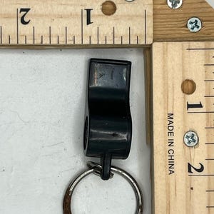 May include: A black plastic whistle with a metal key ring attached. The whistle is positioned next to a wooden ruler marked in inches. The ruler is marked with the text "MADE IN CHINA".