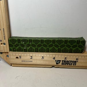 Könnte beinhalten: Eine rechteckige grüne Schachtel mit einem sich wiederholenden Blumenmuster, etwa 15 cm lang. Sie liegt neben einem Holzlineal mit dem Text "MADE IN CHINA" und dem Logo von Tractor Supply Co.