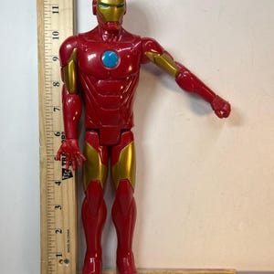 May include: A red and gold Iron Man action figure. The figure has a red body with gold accents on the arms, legs, and helmet. The figure is approximately 12 inches tall.