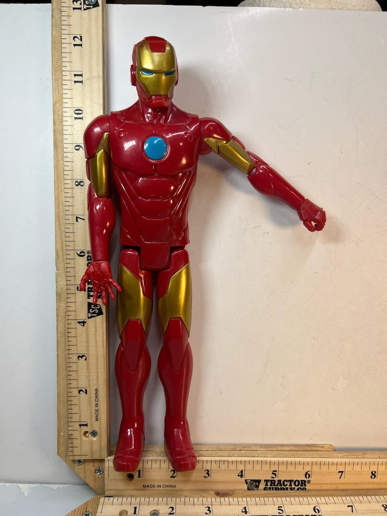 May include: A red and gold Iron Man action figure. The figure has a red body with gold accents on the arms, legs, and helmet. The figure is approximately 12 inches tall.