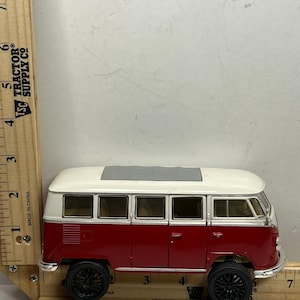 May include: A red and white toy van with black wheels. The van has a gray roof and a white top. The van is approximately 6 inches long. The van is a miniature replica of a classic vehicle.