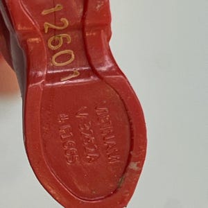 Puede incluir: Primer plano de un objeto de pl&aacute;stico rojo con el texto "1260N" en dorado. Tambi&eacute;n es visible el texto "VIETNAM" y "V-3752A". El objeto tiene forma de zapato y un agujero hexagonal.