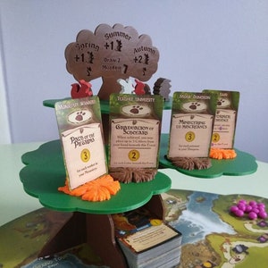Peut inclure: Mise en place d'un jeu de société avec un porte-cartes en forme d'arbre en bois. Le jeu comprend des cartes, des jetons et un plateau de jeu avec des empreintes de pattes et une carte.