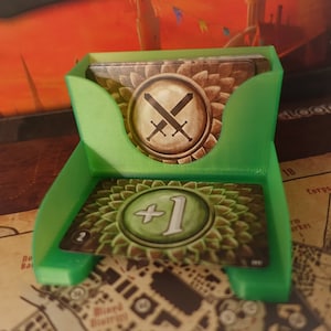 Puede incluir: Un porta tarjetas de plástico verde con dos tarjetas en su interior. La tarjeta superior tiene un fondo marrón con dos espadas cruzadas y un diseño floral verde y marrón. La tarjeta inferior tiene un fondo verde con un círculo verde que contiene un "1" blanco y un diseño floral verde y marrón.