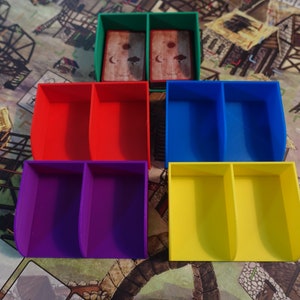 Pu&ograve; includere: Cinque scatole di stoccaggio in plastica con divisori. Le scatole sono verdi, rosse, blu, viola e gialle. Le scatole sono progettate per contenere pezzi di gioco o carte.