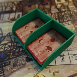Pu&ograve; includere: Porta carte in plastica verde con due scomparti per contenere le carte. Le carte hanno uno sfondo marrone con una grafica di luna, sole e nuvola. Il testo "Event" &egrave; visibile sulle carte.