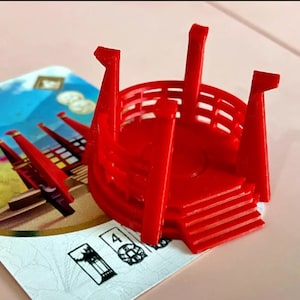 Puede incluir: Una pieza de juego de plástico roja con forma de pagoda con una plataforma circular y cuatro pilares. La pieza está diseñada para un juego de mesa.